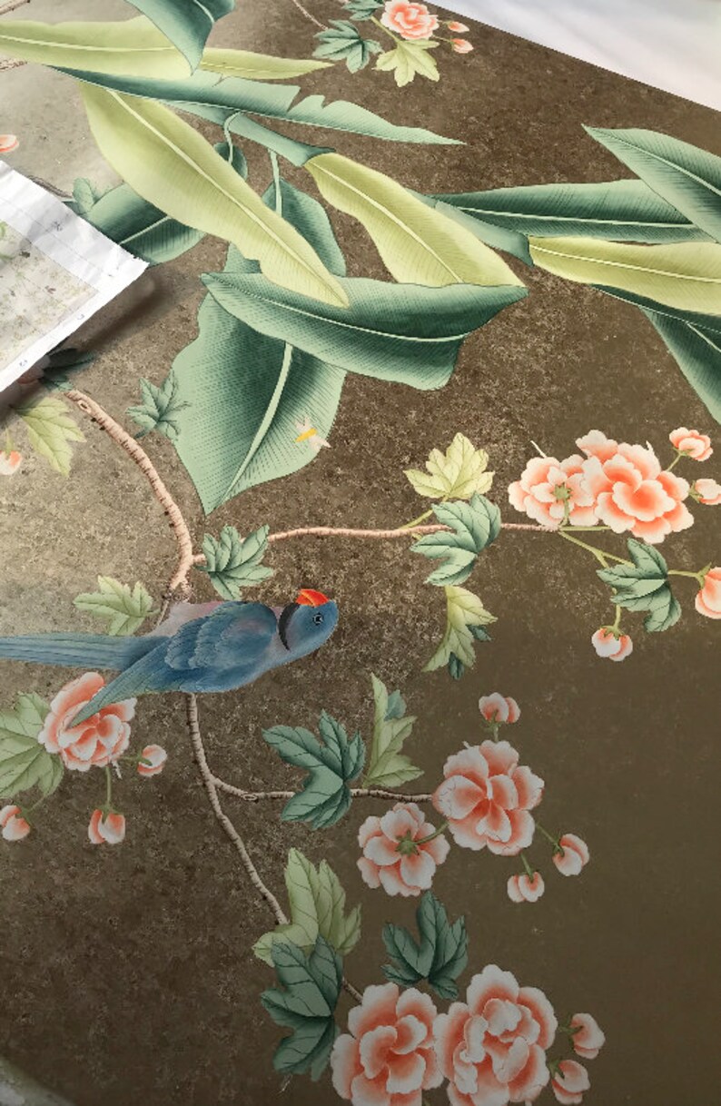 May include: Detailed illustration of a bird and floral design. The artwork features a blue bird with a red head, surrounded by peach-colored flowers and green leaves. The background has a gold-toned, textured appearance.