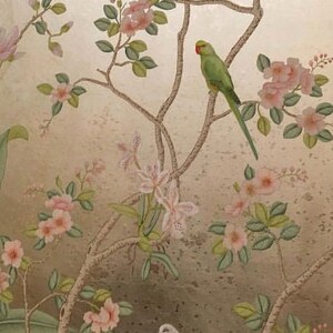 May include: A decorative wallpaper design featuring birds and floral branches. The image showcases a green parrot with a red beak perched on a branch, surrounded by pink blossoms and white birds against a gold background.