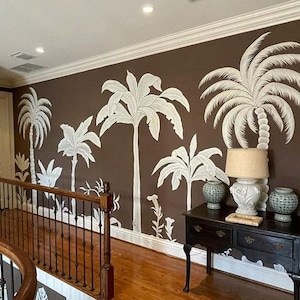 Op de afbeelding: Een gang met een bruine muur met een muurschildering van witte palmbomen. Een donkere houten tafel met een lamp en decoratieve items staat in de hoek van de kamer.