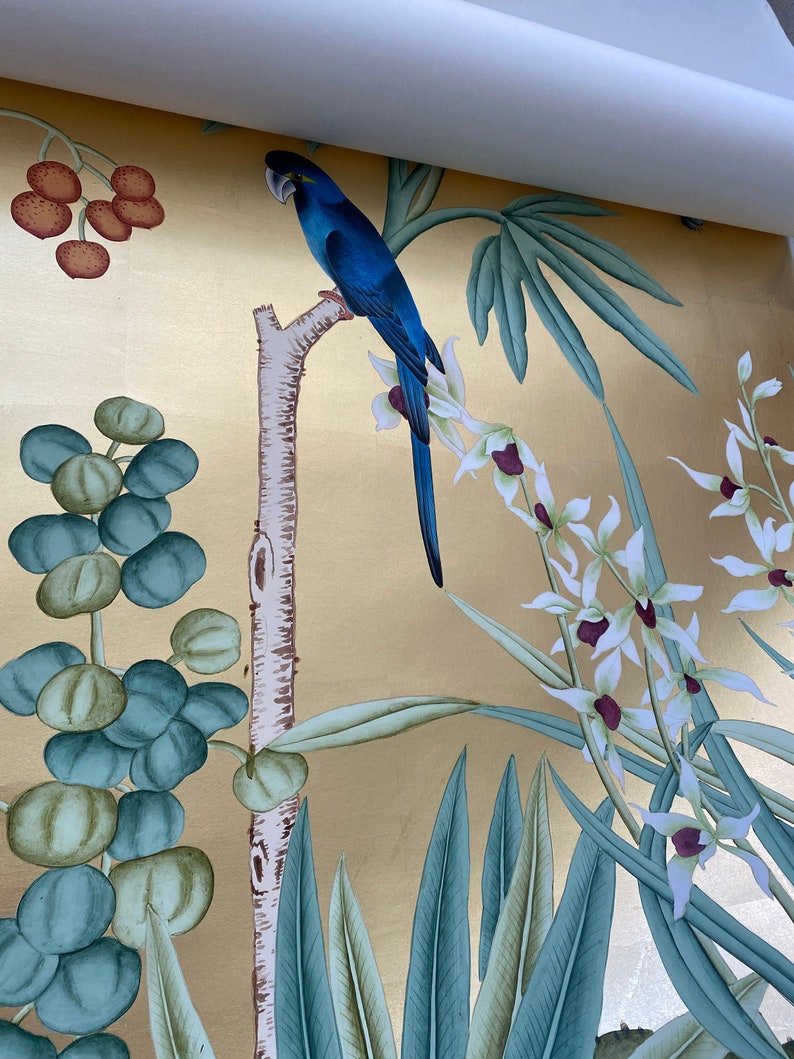May include: A vibrant wallpaper design featuring a blue parrot perched on a tree branch. The background is a gold metallic color, with painted botanical elements including white orchids, green leaves, and red berries. The overall theme is tropical and exotic.