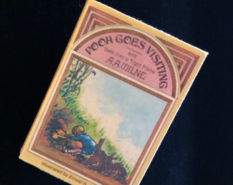 May include: A vintage book cover with a yellow background and a pink circle featuring the text "POOH GOES VISITING and Gets Into a Tight Place A.A.MILNE". The cover features an illustration of Winnie the Pooh and Piglet in a forest setting. The text "Illustrated by Ernest H. Shepard" is at the bottom of the cover.