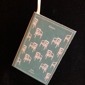 May include: A teal blue book with a white ribbon bookmark. The cover features a repeating pattern of white chairs and the text "Emma" and "Jane Austen".