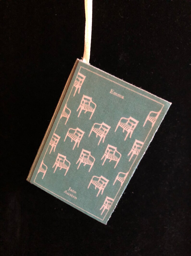 May include: A teal blue book with a white ribbon bookmark. The cover features a repeating pattern of white chairs and the text "Emma" and "Jane Austen".