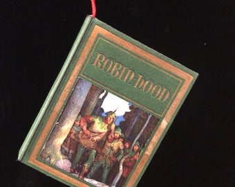 May include: A green book with a gold border and the title "Robin Hood" printed on the cover. The cover features an illustration of Robin Hood and his band of merry men in the forest.
