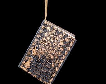 May include: A hanging book titled Pride and Prejudice by Jane Austen, illustrated by Hugh Thomson. The dark blue cover features a gold-coloured peacock design with an elaborate tail pattern that spreads across the front of the hardback book.