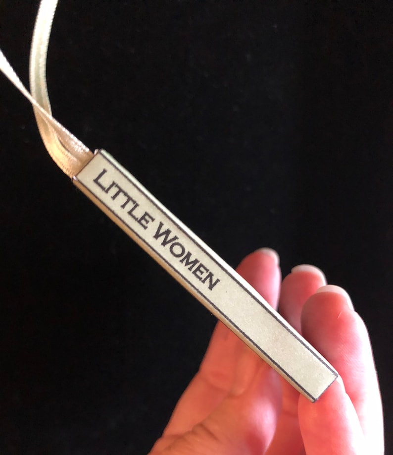 May include: A close-up of a beige bookmark with the text "LITTLE WOMEN" printed in black.