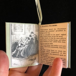 May include: A vintage book with a green cover and a black and white illustration of a group of girls sitting around a table. The book is open to a page with the text "1. Playing Pilgrims." and a passage about Christmas.