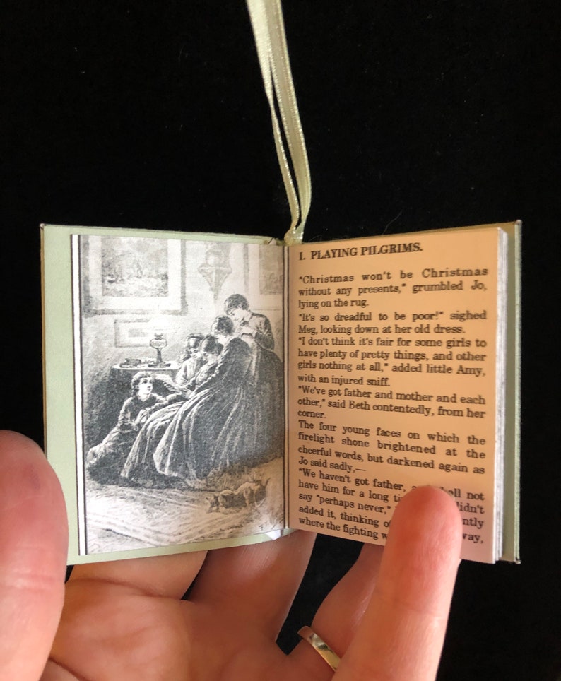 May include: A vintage book with a green cover and a black and white illustration of a group of girls sitting around a table. The book is open to a page with the text "1. Playing Pilgrims." and a passage about Christmas.