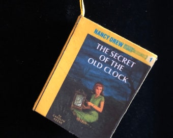 May include: A yellow book with a blue cover and the title "The Secret of the Old Clock" by Carolyn Keene. The book is part of the Nancy Drew Mystery Stories series and is number 1 in the series.