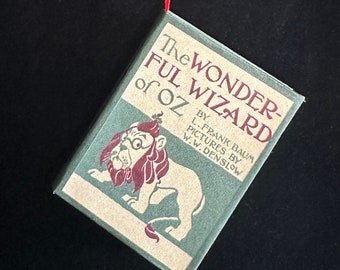 May include: A vintage book cover with a green background and a lion illustration. The title is "The Wonderful Wizard of Oz" by L. Frank Baum with pictures by W.W. Denslow.