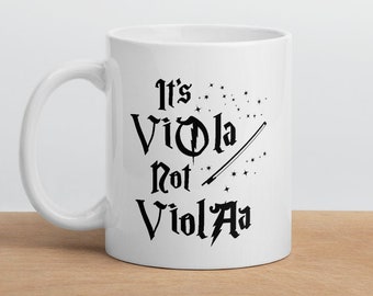 May include: White ceramic mug with a black design that says "It's Viola Not ViolA" with a black violin bow and stars.