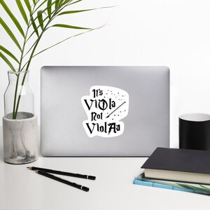 May include: A black and white sticker with the text "It's Viola Not ViolAa" with a wand and stars.