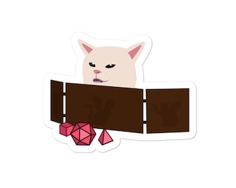 May include: A white cat with a grumpy expression peeks over the top of a brown wooden box with a dragon design.  The box is open and there are several pink dice scattered around it.