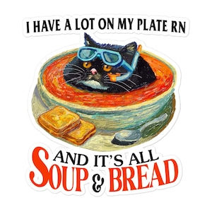 May include: A black cat wearing a snorkel and goggles is submerged in a bowl of tomato soup with two slices of bread on the side. The text "I have a lot on my plate rn and it's all soup & bread" is written on the sticker.