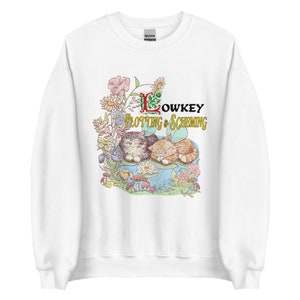 May include: White sweatshirt with a graphic of two cats sleeping on a lily pad surrounded by flowers and mushrooms. The text "Lowkey Plotting & Scheming" is above the cats.