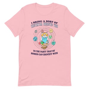 May include: Pink t-shirt with a cartoon cat design. The cat is wearing a blue dress and juggling planets. Text on the shirt reads "I bring a sort of existential nihilistic vibe to the party that my homies can identify with."