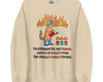 May include: A beige sweatshirt with a cartoon cat wearing a firefighter's helmet and watering flowers. The cat is on fire and the text reads "I'm experiencing the normal amount of anxiety over the things I cannot control."