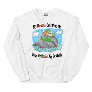 May include: White sweatshirt with a cartoon illustration of two people sitting on a rock in a lake. The text "My Demons Can't Find Me When My Homies Are Beside Me" is printed on the sweatshirt.