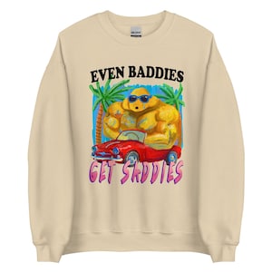 May include: Beige sweatshirt with a graphic of a muscular yellow figure in sunglasses, a red convertible, and palm trees. The text "EVEN BADDIES GET SADDIES" is printed above and below the graphic.