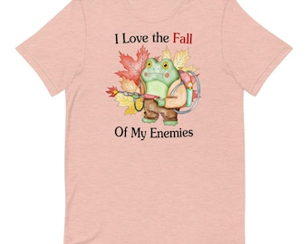 May include: A light pink t-shirt with a cartoon frog wearing a backpack and holding a flamethrower. The text "I Love the Fall of My Enemies" is printed on the shirt.