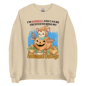 May include: Beige sweatshirt with a cartoon illustration of a monkey-like character inside a carved pumpkin. The text reads "I'M NORMAL AND CAN BE TRUSTED DURING MY Autumnal Outings". The design includes pumpkins and a blue background.