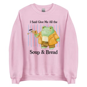 May include: Pink sweatshirt with a cartoon frog holding a gun and the text "I Said Give Me All the Soup & Bread".