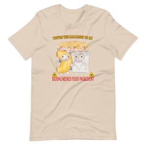 Op de afbeelding: Een beige T-shirt met een afbeelding van twee konijnen die verkleed zijn als macaroni en kaas. De tekst "You're the macaroni to my" en "Bioengineered Food Ingredient" staat op het T-shirt gedrukt.