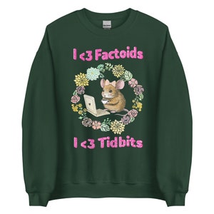Puede incluir: Sudadera verde oscuro con el texto "I <3 Factoids" y "I <3 Tidbits" en letras rosas brillantes. Un ratón con un lazo está dentro de una corona floral, sosteniendo un portátil y una taza.