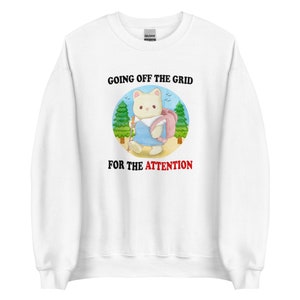 Puede incluir: Sudadera blanca con un gráfico de un gato de dibujos animados con una mochila y haciendo senderismo en el bosque. El texto "Going off the grid for the attention" está impreso en la sudadera.