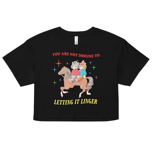 May include: Black cropped t-shirt with a graphic of two cats riding a horse. The text "You are not immune to letting it linger" is printed in red on the shirt.