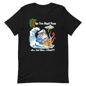 Puede incluir: Camiseta negra con un gráfico blanco de un gato con un sombrero de capitán y dirigiendo un barco a través de un mar tormentoso. El texto "This Too Shall Pass" está por encima del gato y "ok... but like... when???" está por debajo del gato.