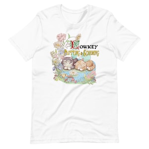 Puede incluir: Camiseta blanca con un gráfico de dos gatos durmiendo en un nenúfar en un estanque. El texto "Lowkey Plotting & Scheming" está por encima de los gatos.