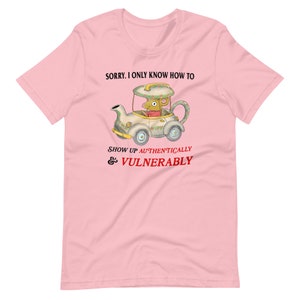 May include: Pink t-shirt featuring a cartoon mouse driving a teapot car. The text on the shirt reads "Sorry, I only know how to show up authentically & vulnerably."
