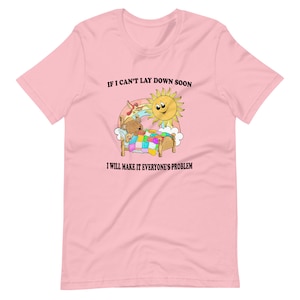 May include: Pink t-shirt with a cartoon illustration of a bear sleeping in a bed with a sun shining above. The text on the shirt reads "If I can't lay down soon I will make it everyone's problem."