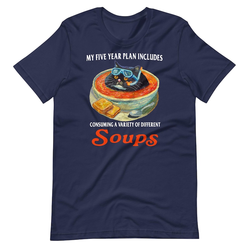 May include: Navy blue t-shirt with a graphic of a black cat wearing goggles in a bowl of soup. The text reads "MY FIVE YEAR PLAN INCLUDES CONSUMING A VARIETY OF DIFFERENT Soups."