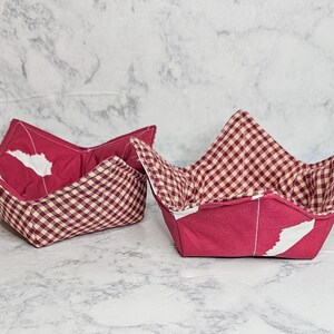 May include: Two red and white gingham fabric bowl cozies. The cozies are folded and ready to use.
