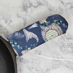 May include: A blue fabric pot holder with a whimsical design featuring a wizard's hat, a door, and other fantasy elements.