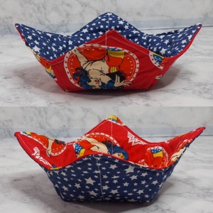 May include: A red and blue fabric bowl with a Wonder Woman design. The bowl is folded and has a star pattern on the inside.