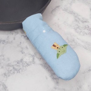 May include: A blue fabric pot holder with a green character wearing a brown hat and a white background with stars.