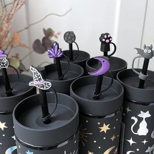 Puede incluir: Conjunto de seis vasos reutilizables negros con una variedad de adornos para pajitas con temática de Halloween. Los adornos incluyen un caldero, un sombrero de bruja, un cristal, un pentagrama, una huella de pata, una luna creciente, un murciélago y un gato. Los vasos tienen un diseño negro y dorado con estrellas y lunas.