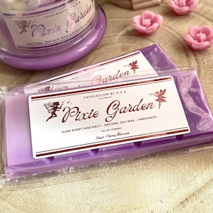 Puede incluir: Fusión de cera de soja púrpura con una etiqueta que dice "CANDLEGLOW BY A.N.A. handmade Pixie Garden PURE SCENT WAX MELT - NATURAL SOY WAX - HANDMADE CA 50 GRAM Scent: Cherry Blossom"