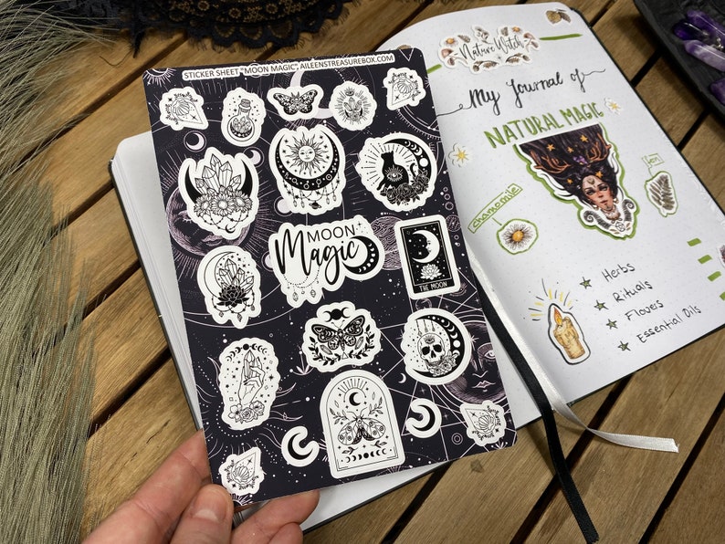 Puede incluir: Una hoja de pegatinas con ilustraciones en blanco y negro de fases lunares, cristales, mariposas y otros elementos m&aacute;gicos. La hoja de pegatinas est&aacute; sobre un fondo negro con estrellas blancas. El texto "Moon Magic" est&aacute; impreso en blanco sobre una pancarta negra. La hoja de pegatinas se titula "Sticker Sheet Moon Magic".