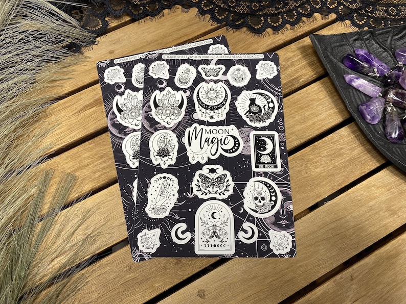 Puede incluir: Dos hojas de pegatinas con fondo negro e ilustraciones blancas de lunas, estrellas, cristales, mariposas y otras im&aacute;genes m&iacute;sticas. El texto "Moon Magic" aparece en una de las hojas.