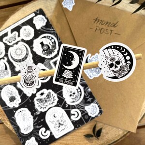 Puede incluir: Un conjunto de pegatinas en blanco y negro con varios dise&ntilde;os de luna, cristal y calavera. Las pegatinas est&aacute;n sobre una superficie de madera e incluyen el texto "Mond - POST - ".