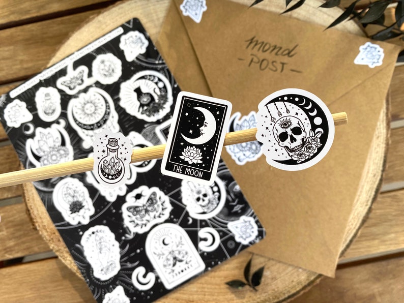 Puede incluir: Un conjunto de pegatinas en blanco y negro con varios dise&ntilde;os de luna, cristal y calavera. Las pegatinas est&aacute;n sobre una superficie de madera e incluyen el texto "Mond - POST - ".