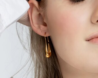 May include: A pair of gold-toned hoop earrings with a unique, slightly curved, teardrop shape.