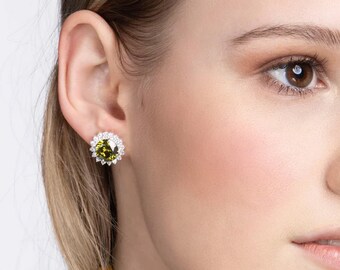 May include: A pair of silver stud earrings with a round green gemstone surrounded by a halo of smaller clear gemstones.