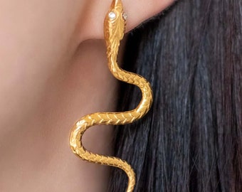May include: Gold snake earrings with a single clear stone on the head of the snake.