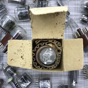 Könnte beinhalten: Draufsicht auf Vintage-Vakuumröhren, einige in ihrer originalen Kartonverpackung. Die Röhren haben Glashüllen und verschiedene interne Komponenten. Die Verpackung ist hellbraun, und die Röhren sind auf einer hellgrauen Oberfläche verstreut.