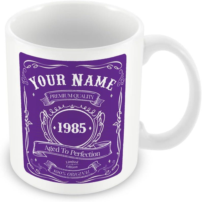 Pu&ograve; includere: Tazza in ceramica bianca con un design viola. Il design presenta un'etichetta in stile vintage con il testo "YOUR NAME", "PREMIUM QUALITY", "1985", "Aged To Perfection", "Limited Edition" e "100% ORIGINAL".